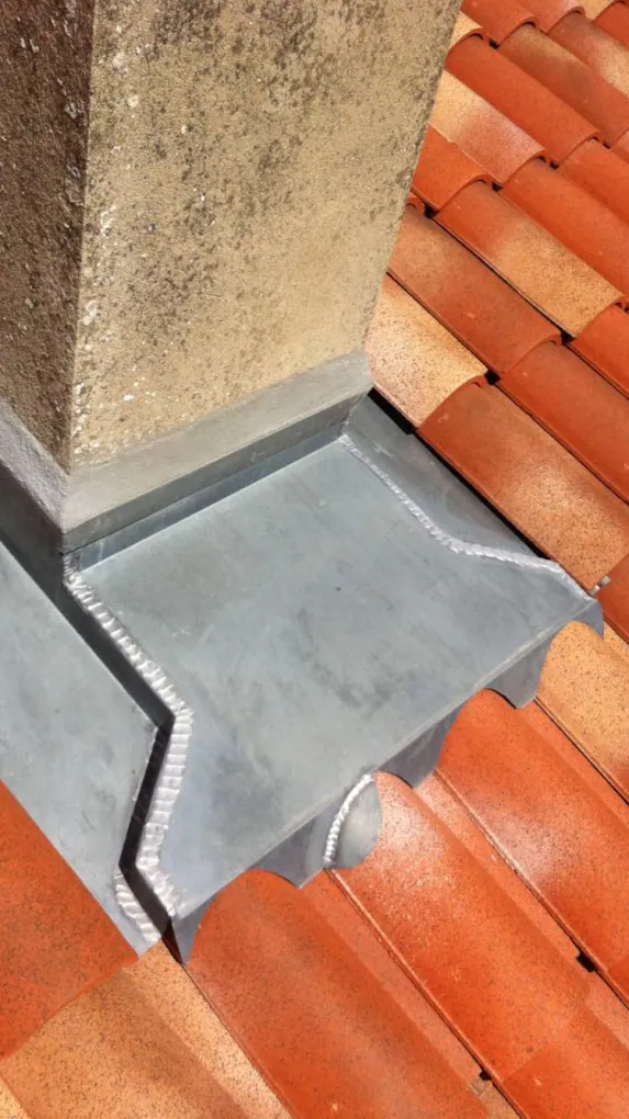 Pièce de zinguerie façonnée sur mesure et posée sur une toiture en tuiles